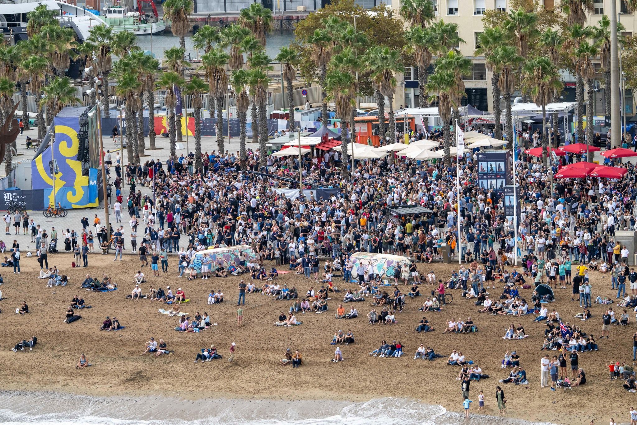 Große Menschenmenge versammelte sich in der Nähe des Strandes mit Palmen und Veranstaltungsständen im Hintergrund