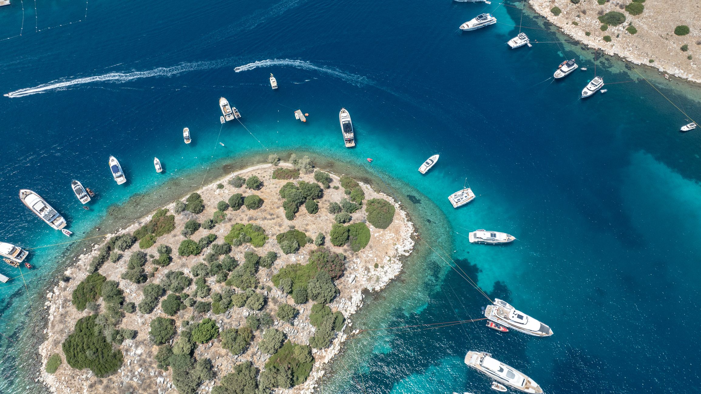 Luxury yachts anchored near a pristine island, surrounded by crystal-clear waters and a stunning coastal landscape.