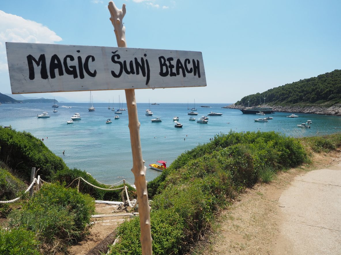 A sign saying Sunj Beach with anchored boats