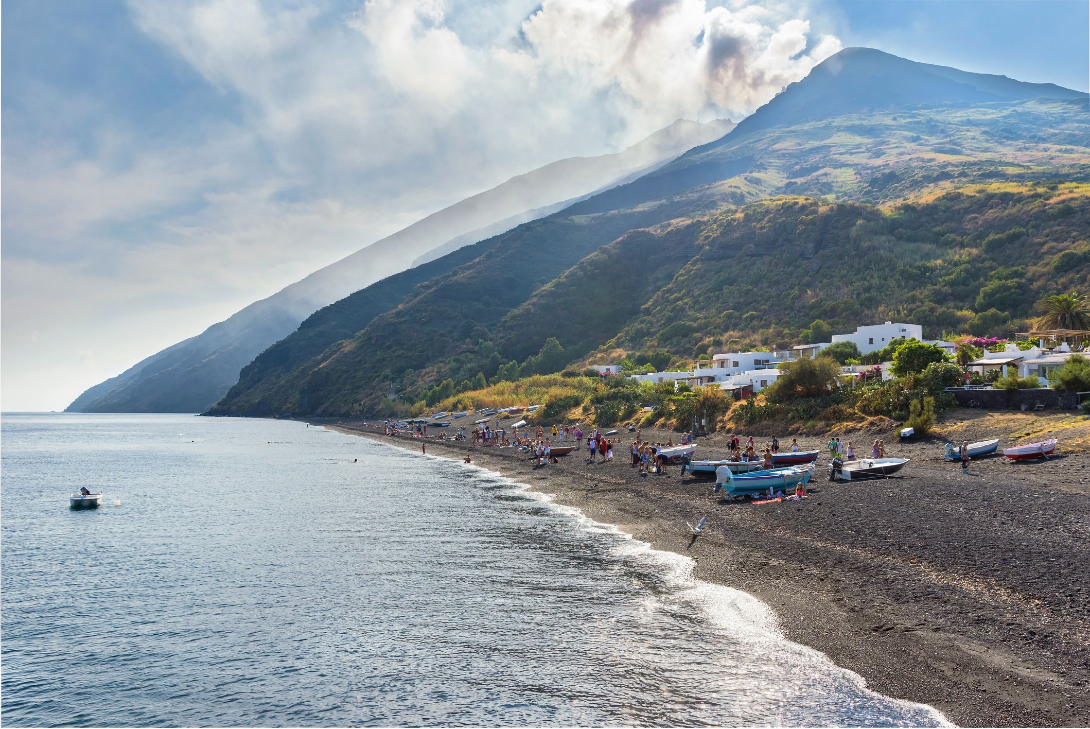People relax on black volcanic beach with Stromboli volcano in the background