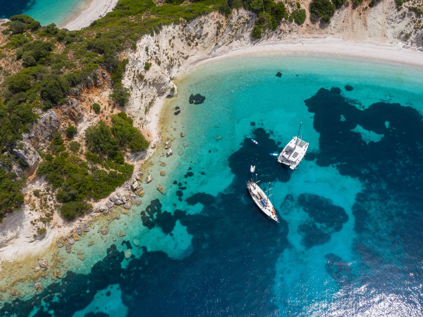 Sailboat and catamaran cruising across a calm blue sea