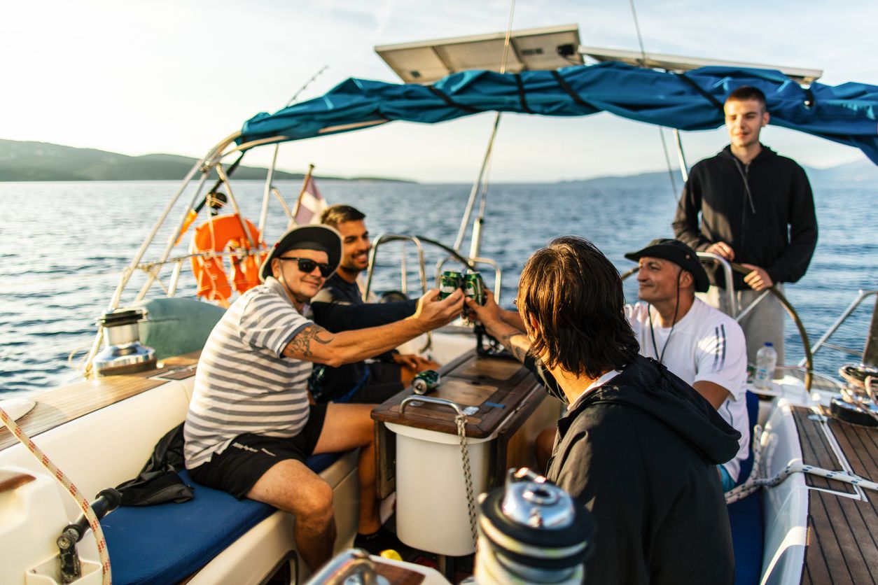 Group of men and women enjoy party drinking champagne with talking together while catamaran boat sailing at summer sunset. Male and female relax outdoor lifestyle on sail yacht tropical travel vacation