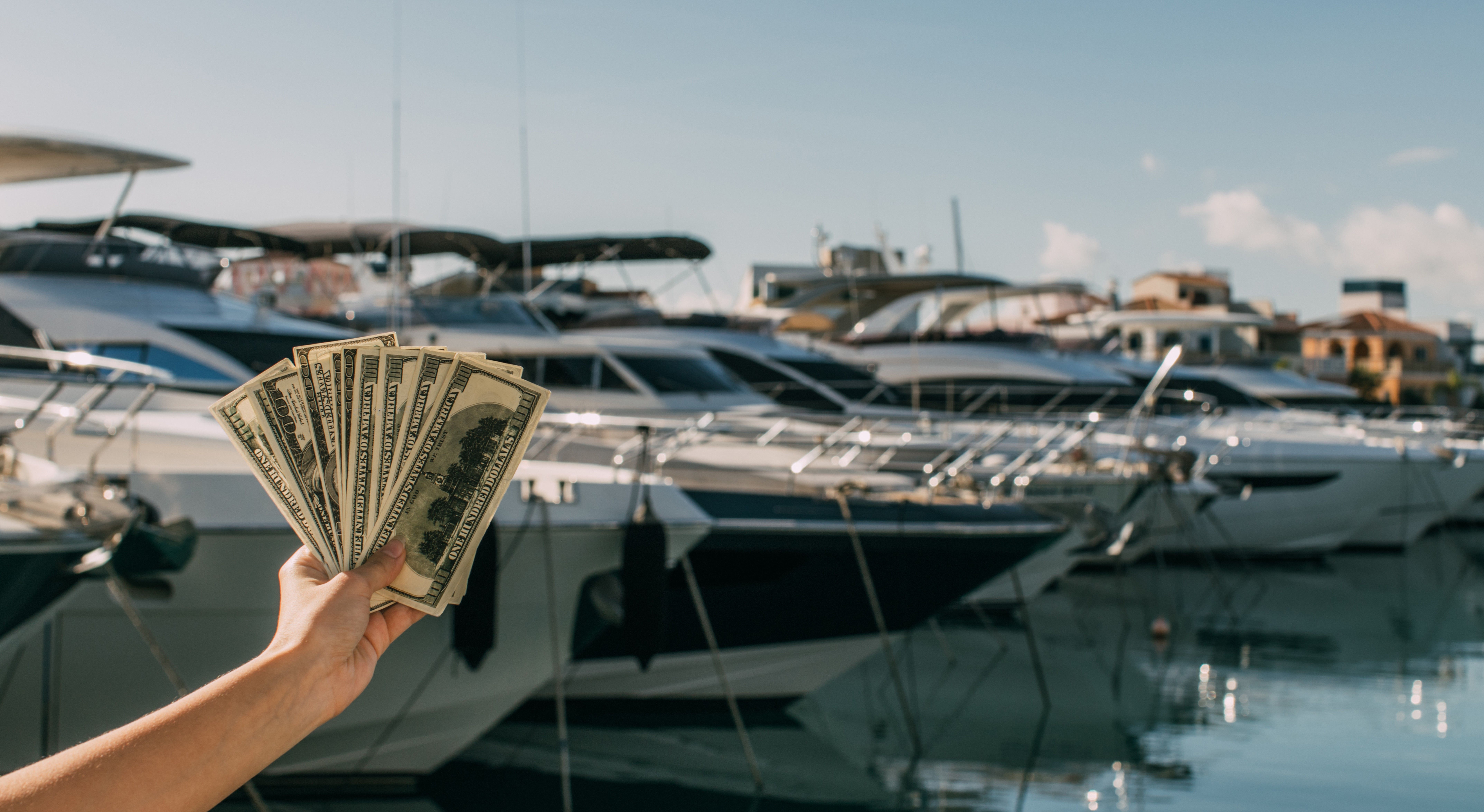 Ruka drží peniaze v maríne pred jachtami