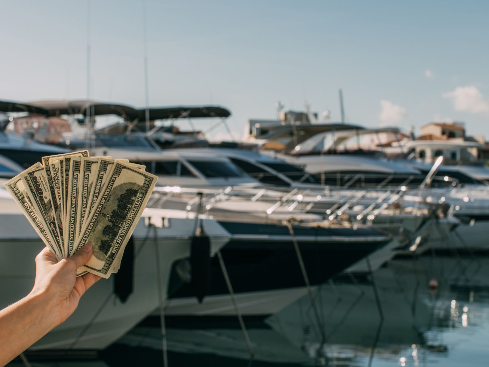 Hand holding money in marina in front of yachts.